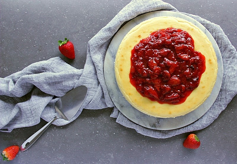 Whole classic cheesecake with strawberry sauce.