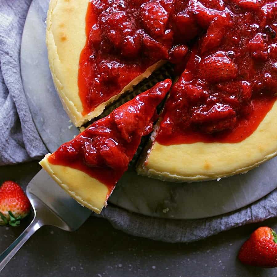 whole classic cheesecake with strawberry sauce, one slice is being removed.