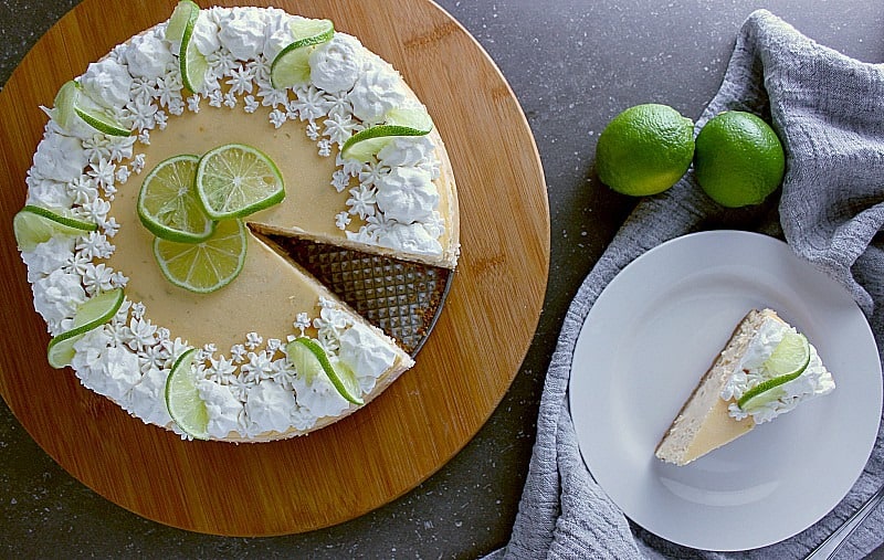 Top of the lime cheesecake decorated with fresh whipped cream and lime slices. One slice is removed and served on a plate.