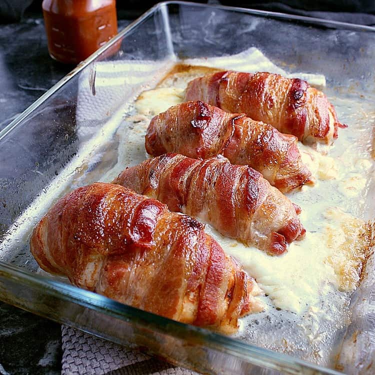 Four bacon wrapped stuffed chicken breasts in a baking pan, fresh from the oven.
