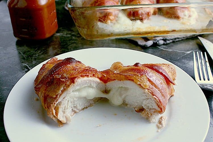 Stuffed chicken breast on a plate, sliced in half, cheese pouring from the center.