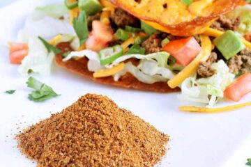 A pile of keto taco seasoning in front of two keto tacos.