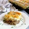 Slice of Keto Shepherd's Pie on a plate with the baking dish in the background. It is garnished with fresh italian parsley.