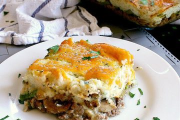 Slice of Keto Shepherd's Pie on a plate with the baking dish in the background. It is garnished with fresh italian parsley.