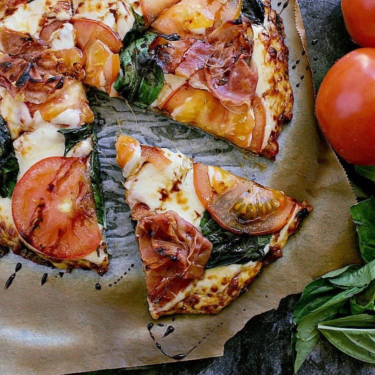 Keto Chicken Pizza Crust made with sugar free pizza sauce, topped with prosciutto and basil; with one slice removed.