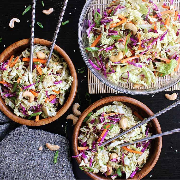 Two small bowls of low carb asian slaw, next to a larger serving bowl.