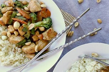 Plate of low carb peanut chicken with cauliflower rice and garnished with peanuts and chopsticks.