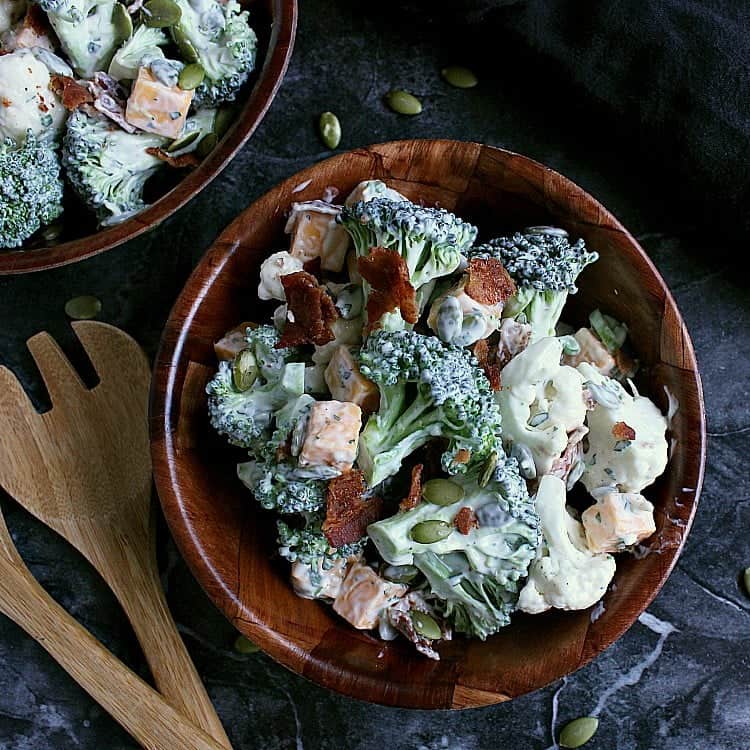 Single bowl of ranch cauliflower broccoli salad with bacon and cheese, with a second bowl of salad in the corner.