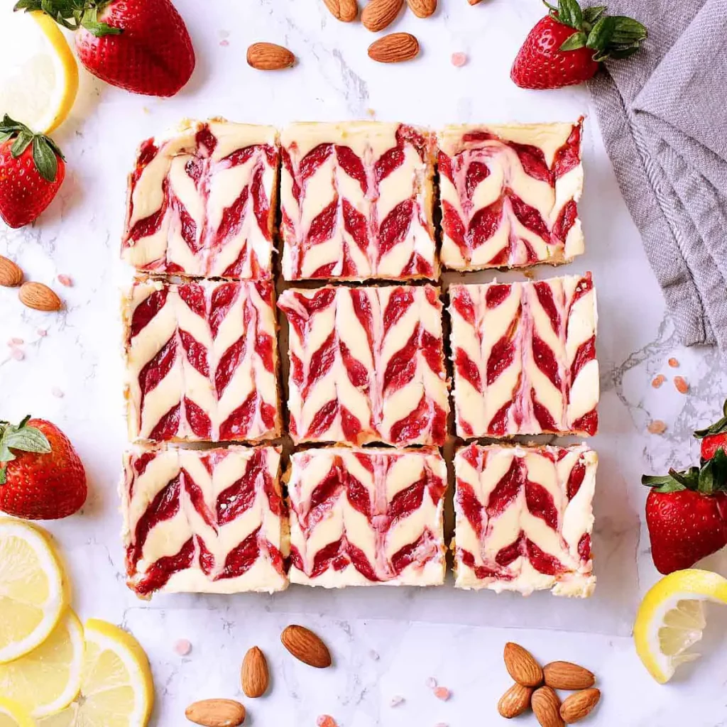 Strawberry Swirl Low Carb Cheesecake Bars, sliced into 9, surrounded by fresh strawberry and lemon slices.