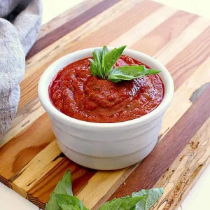 White bowl of sugar free pizza sauce, garnished with fresh basil, all ready to be spread on some pizza!