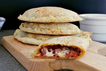 Stack of keto calzones with a half calzone cut in half to show the meat and cheese inside.
