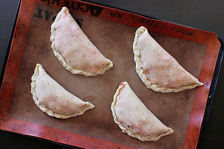 Four keto calzones on a baking sheet, ready to be placed inside the oven for baking.