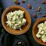 Two bowls of low carb curry chicken salad in wooden bowls. A garnish of pecans and cilantro is spread around the bowls.