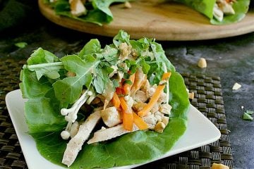 Single keto chicken lettuce wrap on a small plate with the platter of wraps behind.