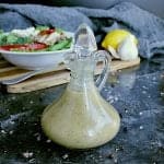 Glass dressing jar with keto Italian dressing. A fresh green salad is in the background with a lemon and some garlic.