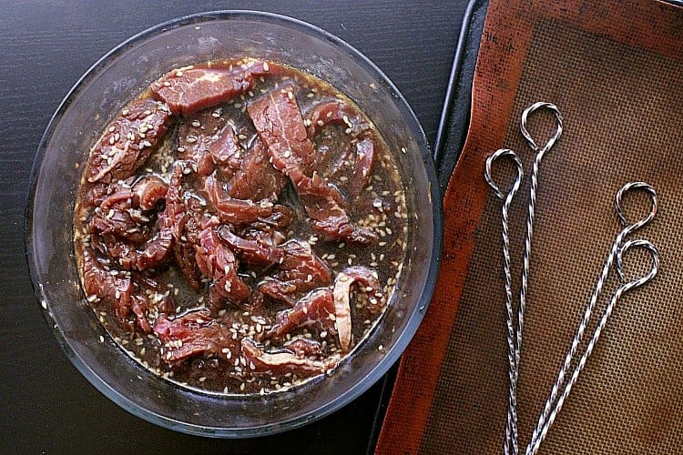 Thin ribbons of beef marinating in a bowl of teriyaki sauce.