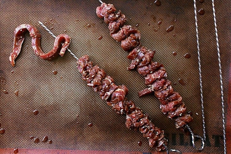 Loading up skewers with marinated slices of beef.