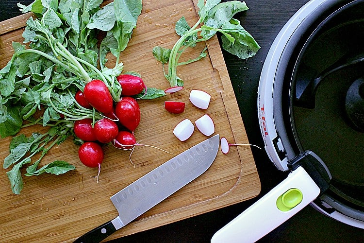 Washed radishes on a cutting board with a knife, next to an acti-fry. One radish has been cut into quarters.