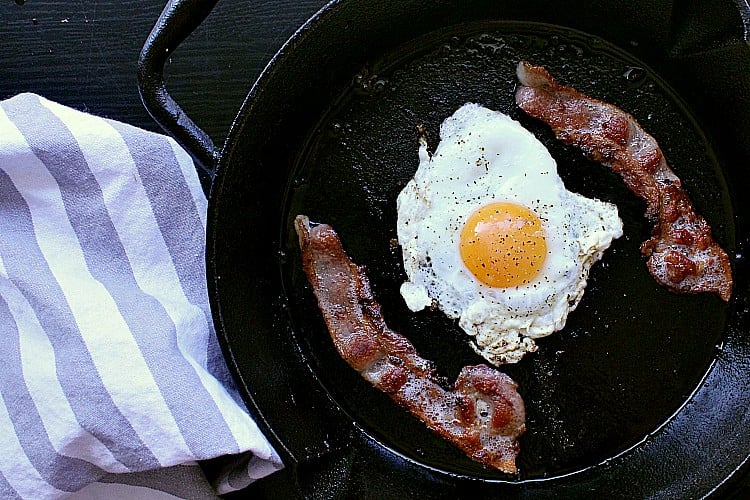 Skillet with two slices of bacon and an egg in the center.