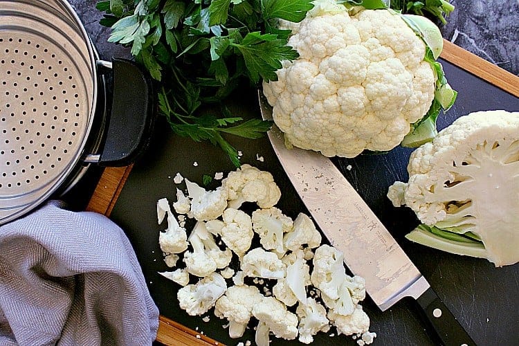 Cutting board with chopped up cauliflower, ready to be added to a steamer.