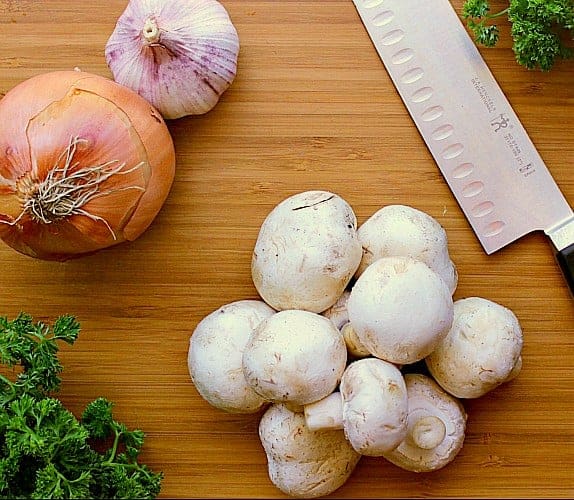 Cutting board with mushrooms, onion and garlic.