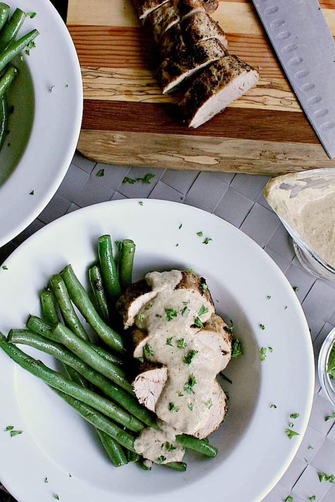 Sliced pork tenderloin next to fried green beans and covered in keto mushroom sauce.