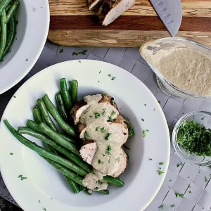 Plate with green beans and sliced pork loin, covered in mushroom sauce.