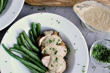 Plate with green beans and sliced pork loin, covered in mushroom sauce.