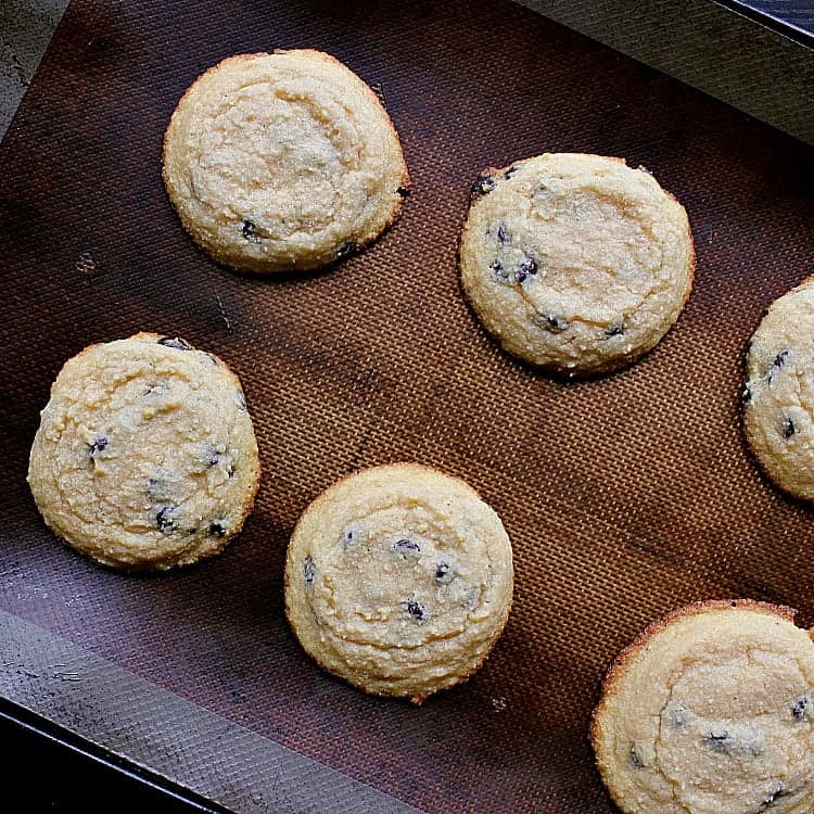 6 freshly baked keto chocolate chip cookies cooling on a baking sheet.