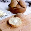 keto dinner roll sliced open with some butter melting. Bowl of rolls in the background next to butter.