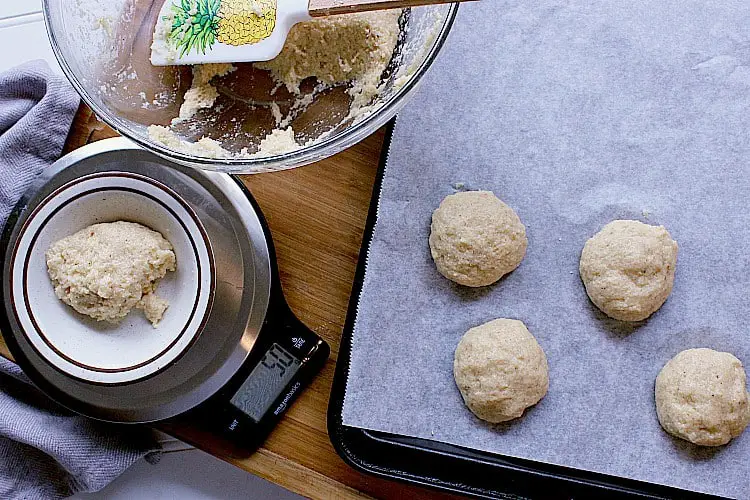 Measuring out buns using a scale. Four portions of batter shaped into balls and placed evenly on a baking sheet.