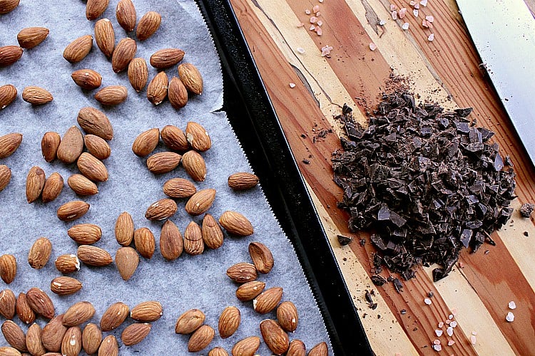 Baking sheet with roasted almonds next to a pile if chopped chocolate.