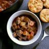 Bowl of low carb beef stew next to the pot of stew and some low carb biscuits.