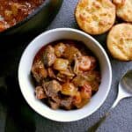 Bowl of low carb beef stew next to the pot of stew and some low carb biscuits.
