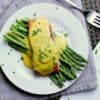 Plate with steamed asparagus and salmon, covered in keto hollandaise sauce and garnished with chives.