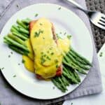 Plate with steamed asparagus and salmon, covered in keto hollandaise sauce and garnished with chives.