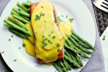 Plate with steamed asparagus and salmon, covered in keto hollandaise sauce and garnished with chives.