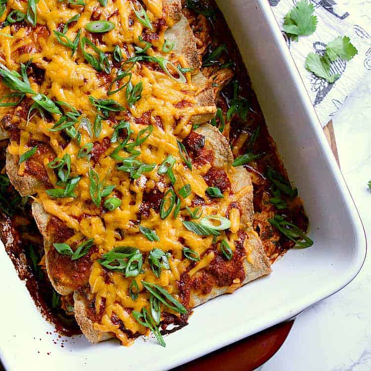 Baking dish with 8 keto enchiladas, covered in melted cheese and green onion.