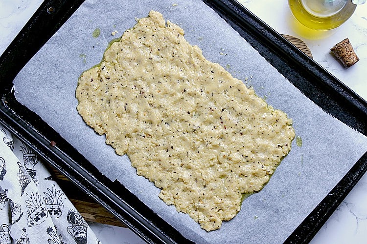 Baking sheet with cheesy keto flatbread dough spread out on it.