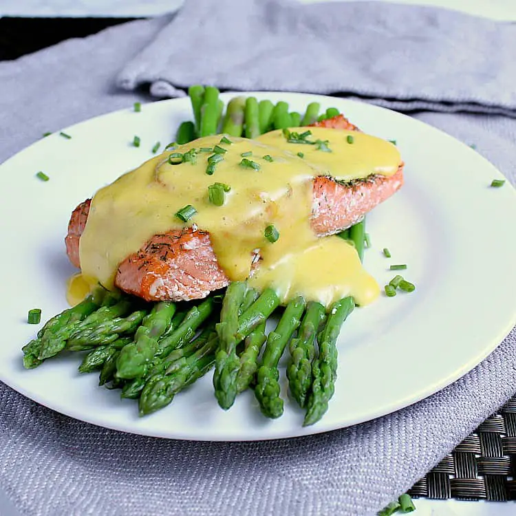 Plate with steamed asparagus and salmon, covered in keto hollandaise sauce and garnished with chives.