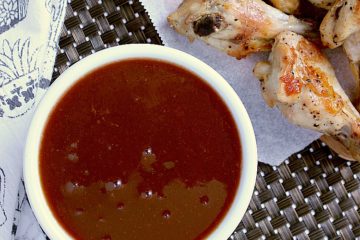 Bowl of keto sweet and sour sauce, next to a platter of chicken wings.