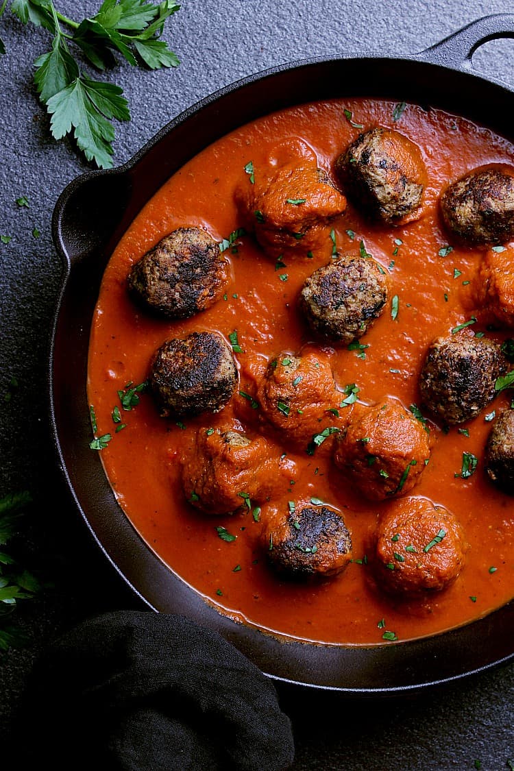 Cast iron skillet with cooked meatballs, hot marinara sauce and garnished with fresh parsley.