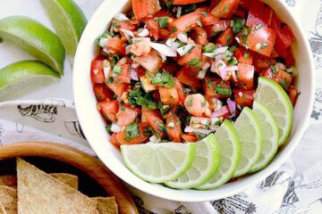 A white bowl with Keto pico de gallo, and sliced limes on top, next to a bowl of Keto chips.