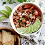 Bowl of keto pico de gallo garnished with fresh lime slices, besides a bowl of low carb baked tortilla chips.