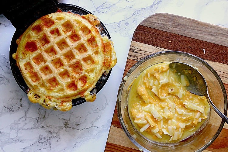 First keto chaffle is cooked, next to a dish with the remaining egg mixture.