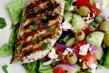 A white bowl with chopped romaine, greek salad and a piece of grilled keto greek chicken.