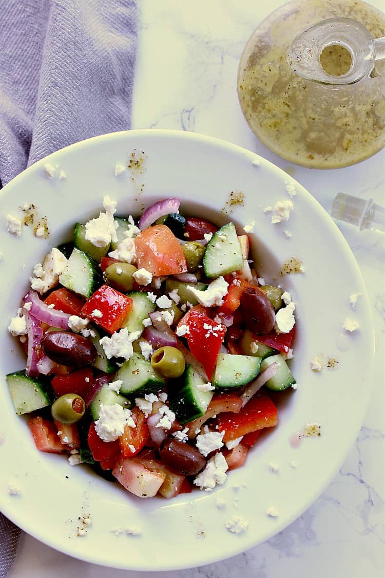 White bowl with greek salad which has been tossed in the keto dressing. A jar of the dressing is beside the bowl.