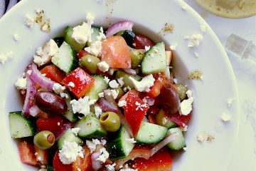 White bowl with greek salad which has been tossed in the keto dressing. A jar of the dressing is beside the bowl.