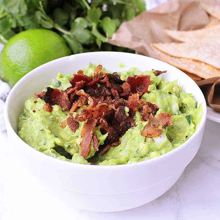 A white bowl with Keto Guacamole, garnished with crisp bacon.