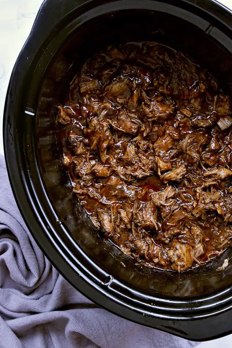 Slow cooker with pulled pork smothered in bbq sauce, ready to be served.